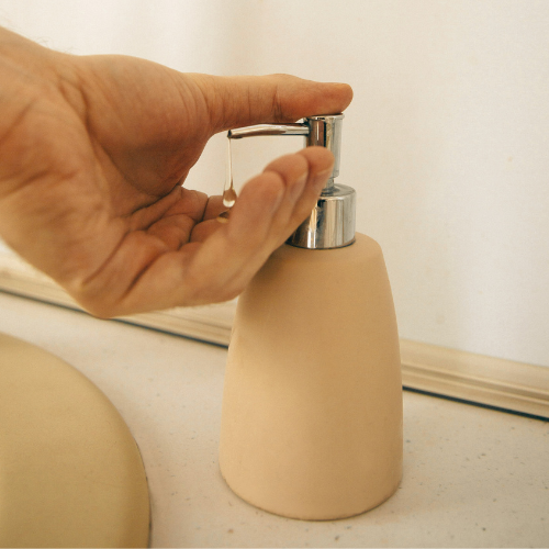 A hand dispensing liquid soap from a beige coloured container with a silver metal pump