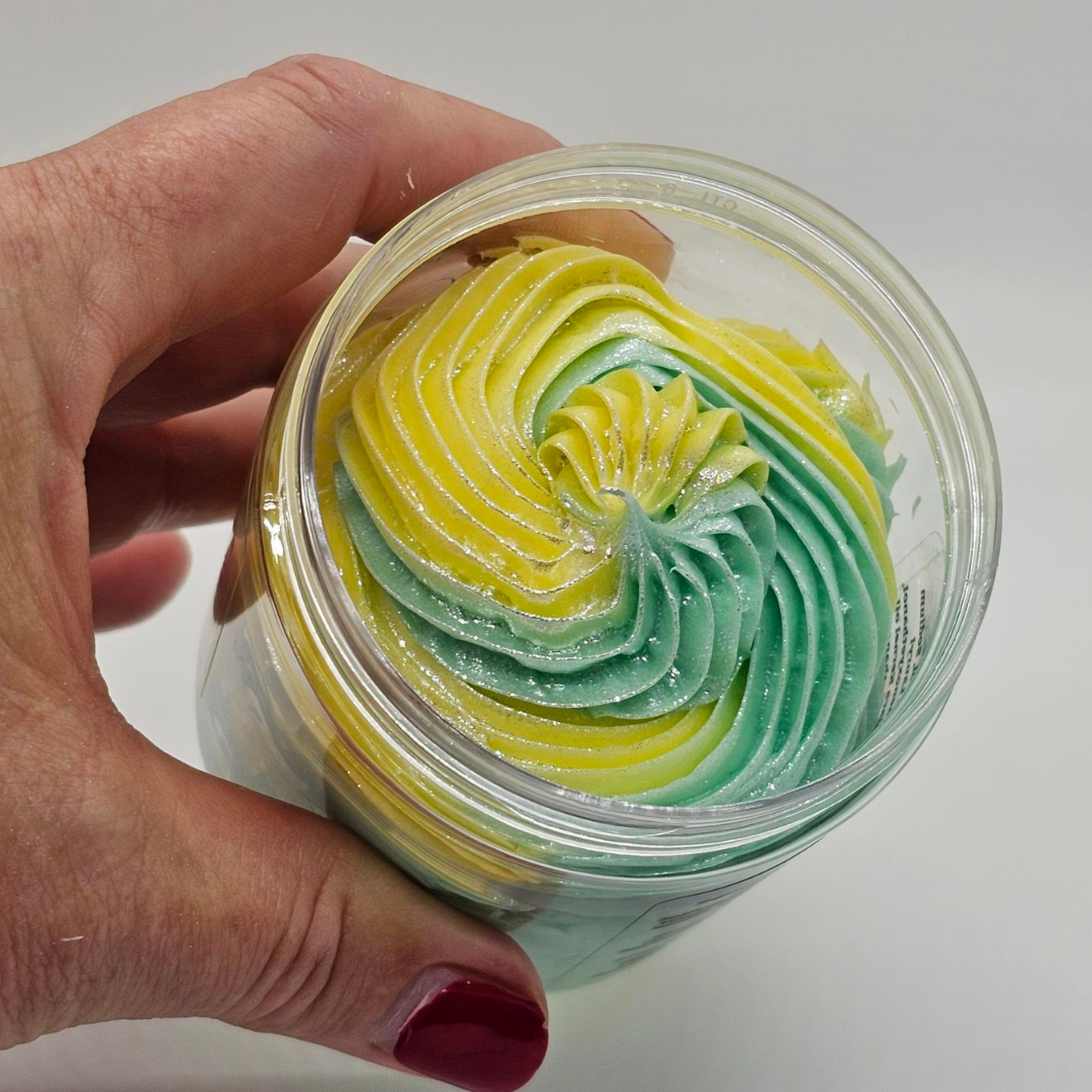 Hand holding a container of layered green and yellow whipped and piped soap base
