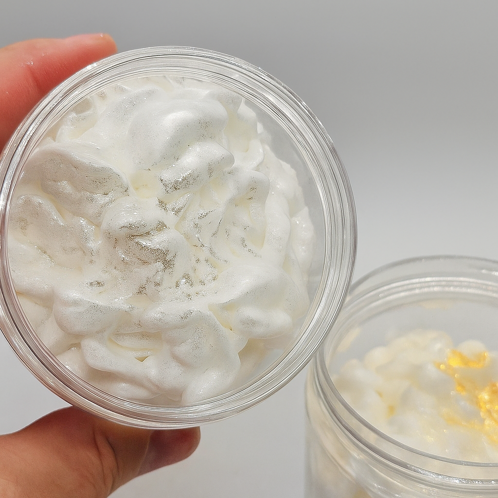 Hand holding a container of whipped mousse soap with visible glitter, against a neutral background.