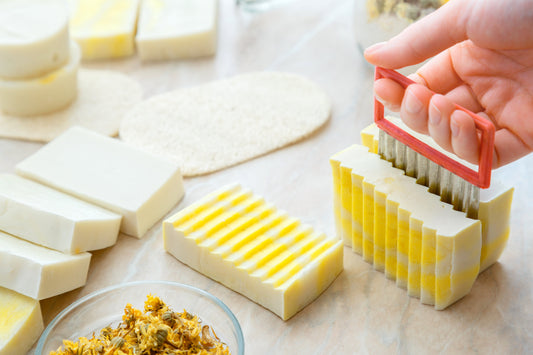 A person cutting handmade soap bars with a crinkle cutter on a light surface, next to other finished soap products.