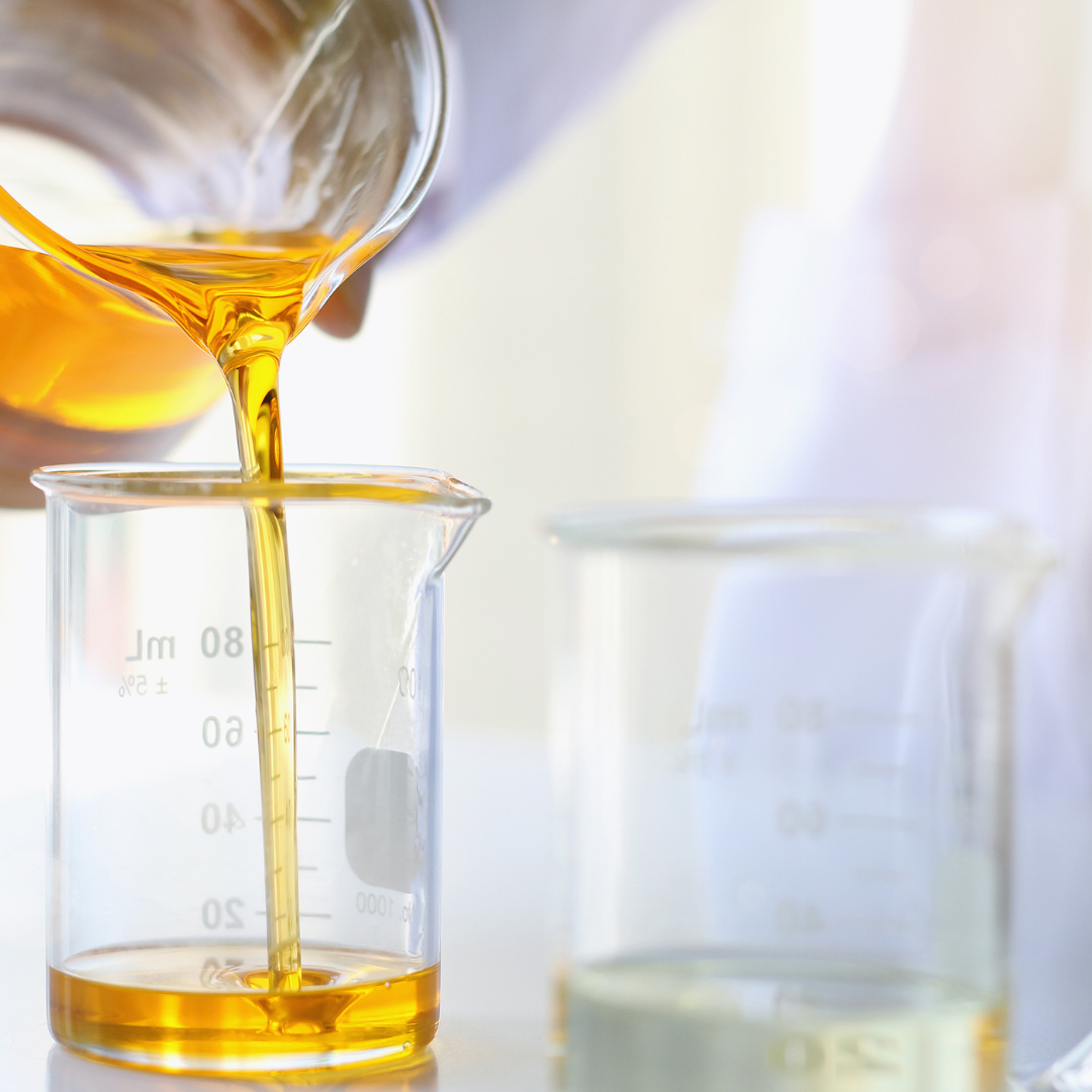 Cosmetic oil being poured from a beaker into a measuring container for cosmetic formulating