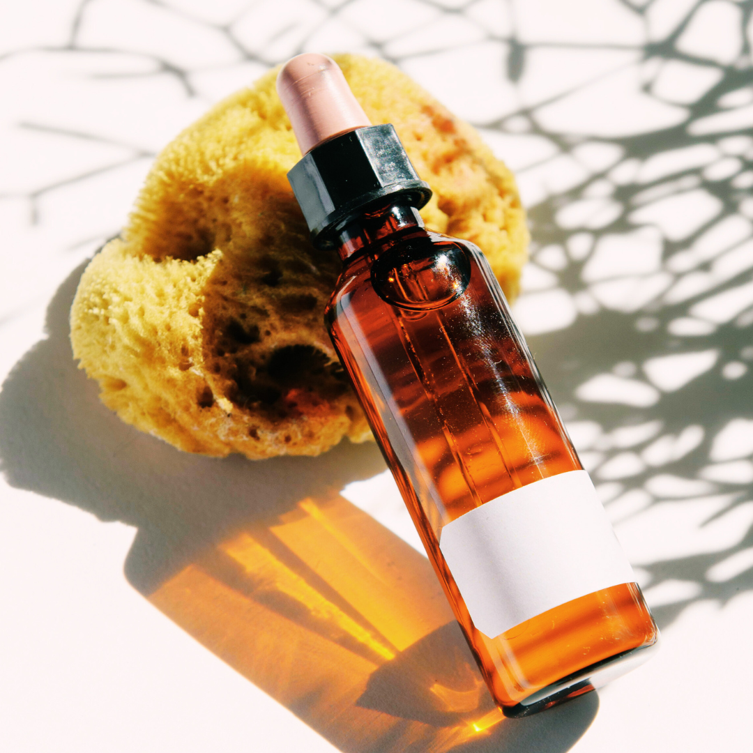 Amber glass dropper with Moringa body Oil made with a CPSR from cosmetic safety solutions with a natural sponge on a light background