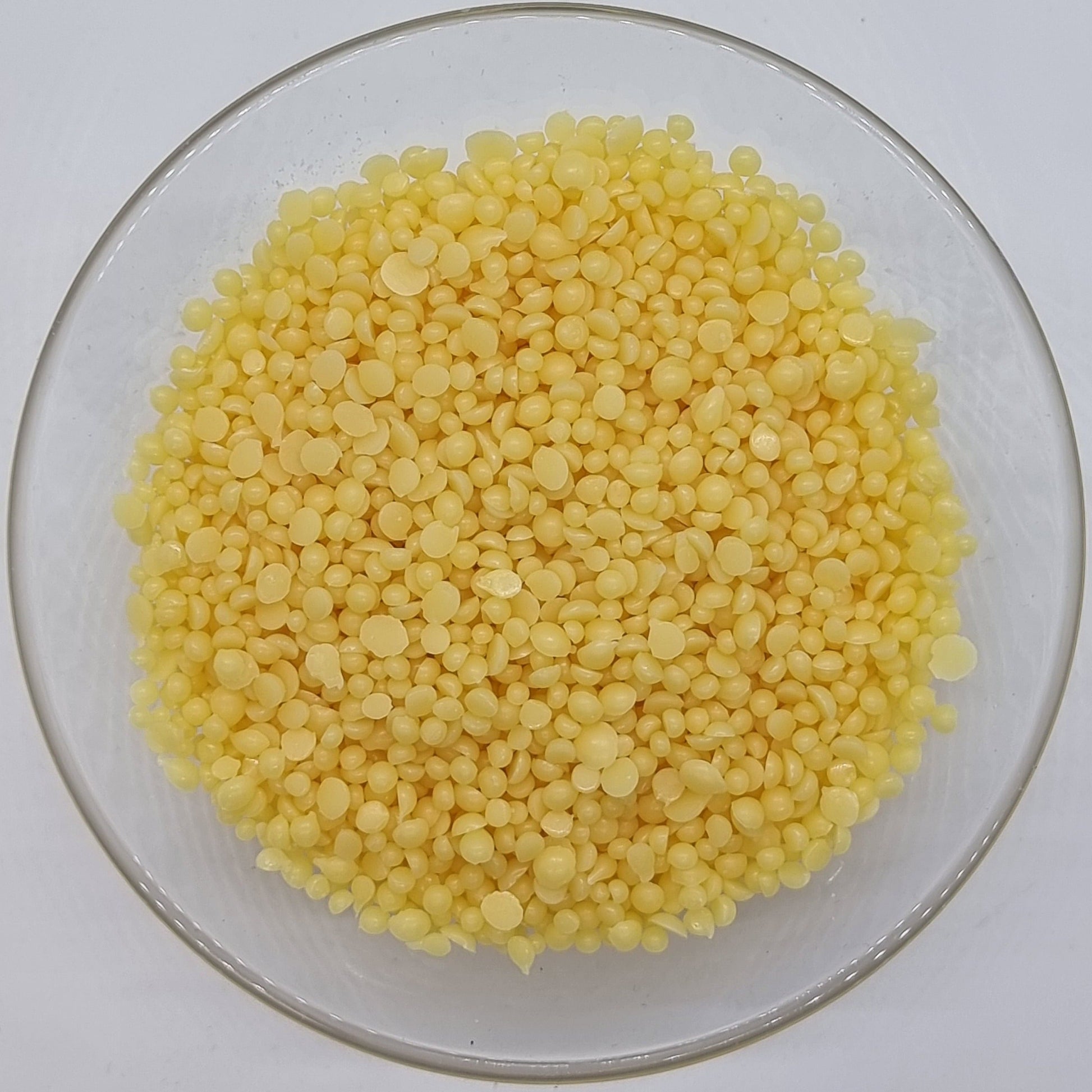 glass bowl containing lots of irregular round shaped with flat back pellets of Candelilla wax, a vegetable substitute for beeswax, suitable for vegans and widely used in soap and cosmetic making recipes.