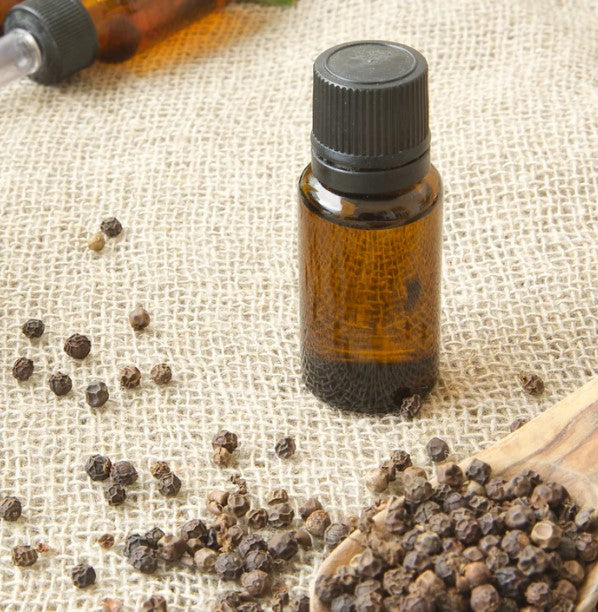 A bottle of pure essential oil with black peppercorns.

