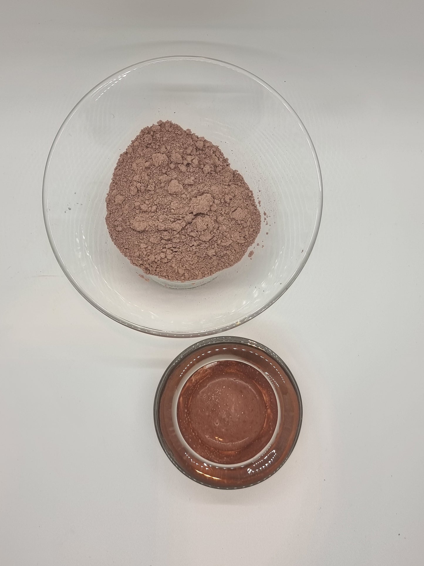 two glass bowls one containing fine french pink clay dry powder, the other pink clay paste.